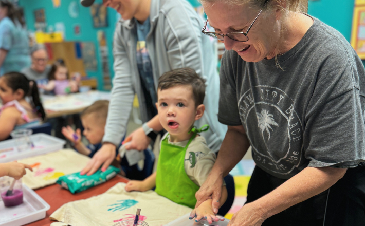 Story Hour - patron helping her child make a handprint with paint on a canvas